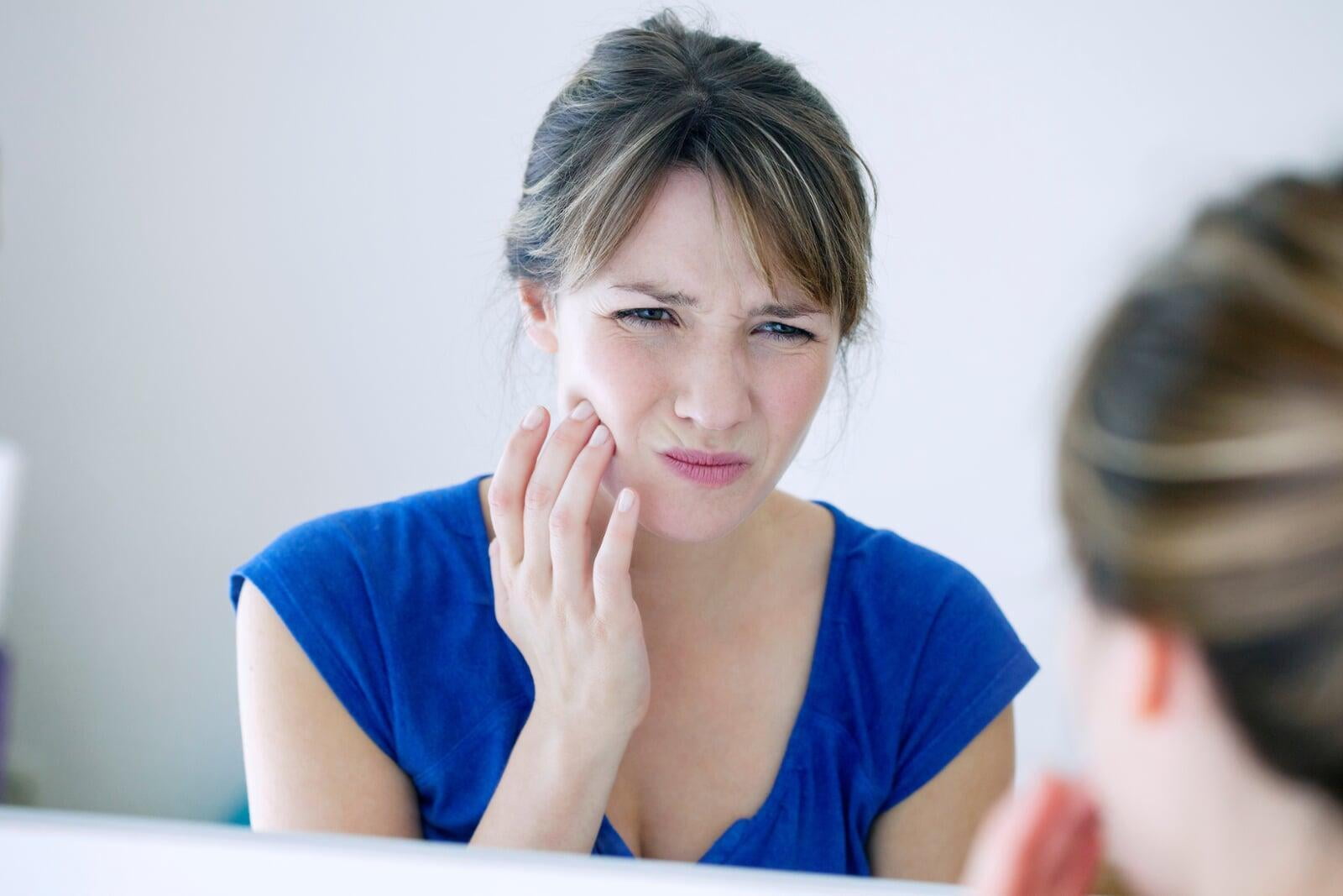 A woman who grinds her teeth in her sleep holds her jaw and thinks about getting a bite splint from her Chch dental hygienist 